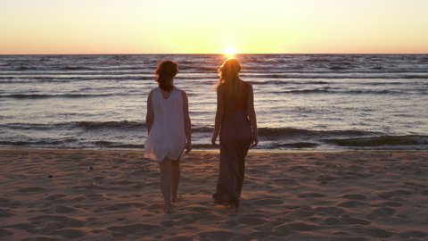 Two young lesbian women walk together towards sunset