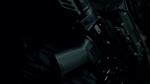 An assault rifle with a telescopic sight hanging on a belt on a black background