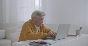 Senior mature older woman typing a message on the keyboard, online webinar on laptop computer remote working or social distance learning from home. 60s-80s businesswoman