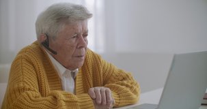 Senior woman with laptop computer calling on smartphone at home. Old woman having a video call on the laptop smiling and talking happily indoors in a cozy apartment. doctor video calling older patient