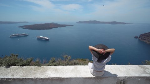 Elegant woman with hat enjoying view of Santorini, Greece Landscape with view of volcano, cruiser boats and caldera