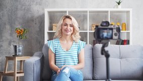 Young and attractive woman is recording video blog with a camera. Girl is sitting at home and vlogging.