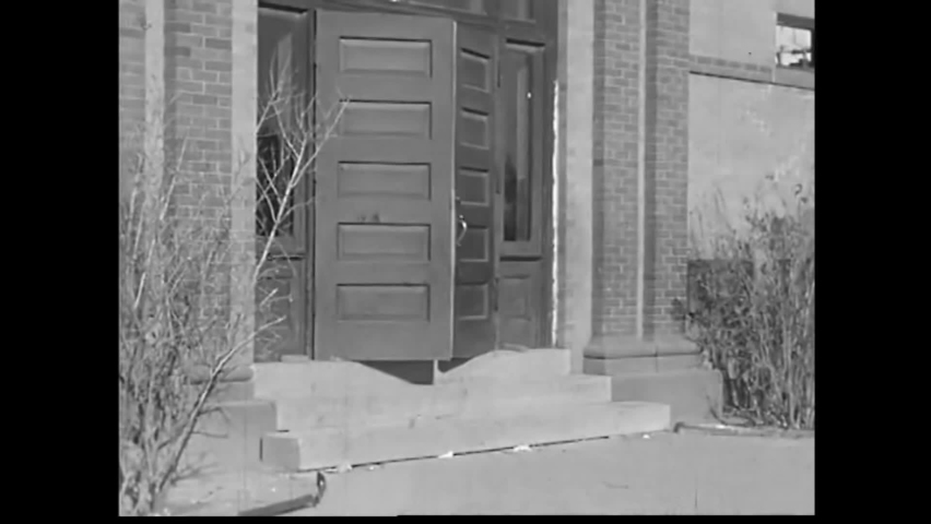 CIRCA 1930s - School children leave the building in rows whilst a pair hold the doors open for them all to leave in South Dakota in 1938.