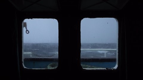 Storm view from cabin window. Strong side pitching. Sea view from ship windows. Waves crash against side and spray covers sky. Very strong storm. High waves with foam are visible through portholes.