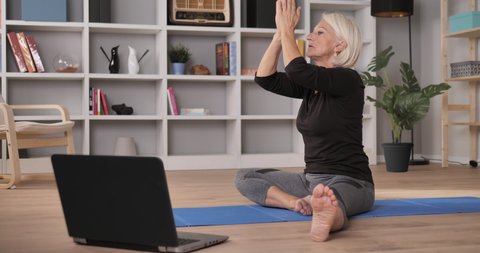 mature woman exercise workout at home online personal trainer. wellness healthy lifestyle elderly woman stretching yoga watching an online course on the computer.