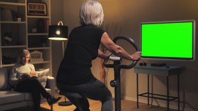 old woman exercise bike watching green screen tv television,healthy lifestyle in isolation elderly lady training work out on stationary bike at home watches chroma key display
