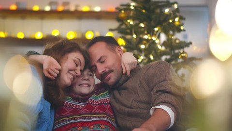 Happy mom, dad and preteen son embracing relaxing on couch in apartment decorated for christmas. Portrait of loving parents with cute boy hugging celebrating new year together