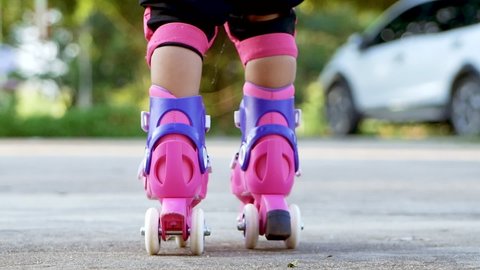 Little girl wearing protection pads and safety helmet learning to roller skate in summer park. Active outdoor sport for kids. Close-up legs