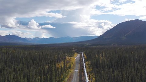 Drone follows high above trans-Alaska pipeline on September autumn day with fall colors and sun with distant mountains.