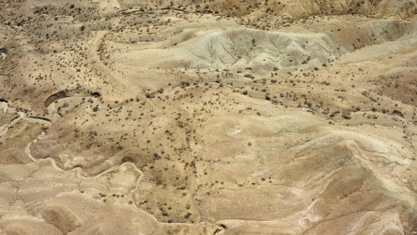 Drone view flying over the dry sandy mountains in the Rainbow Basin part of the Mojave Desert; small scrub bushes dot the landscape.