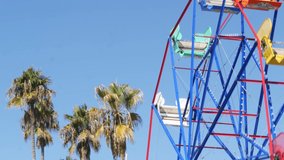 Classic vivid summertime, fun and childhood symbol, green tropical palm tree leaves. Iconic colorful retro ferris wheel attraction. Newport, california pacific ocean beach resort near Los Angeles USA.