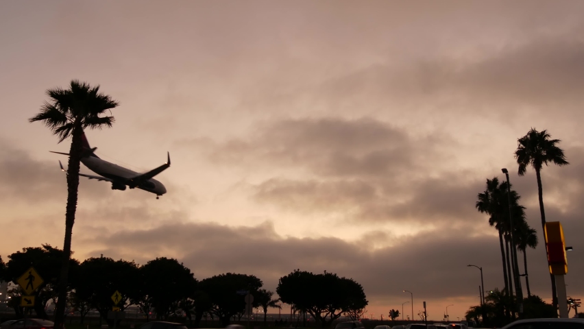 Airplane landing in LAX airport at sunset, Los Angeles, California USA. Passenger flight or cargo plane silhouette, dramatic cloudscape. Aircraft arrival to airfield. International transport flying. Royalty-Free Stock Footage #1063219936