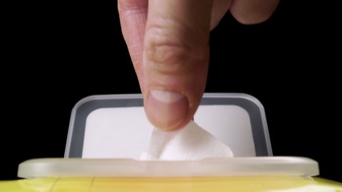 Hand takes a wet napkin from a yellow plastic pack on a black background close up. Disinfection from virus bacteria