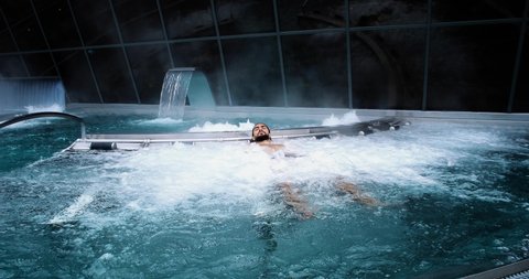 Man relaxing in a spa, he is lying in the water. Perfect leisure activity in winter holidays 4K