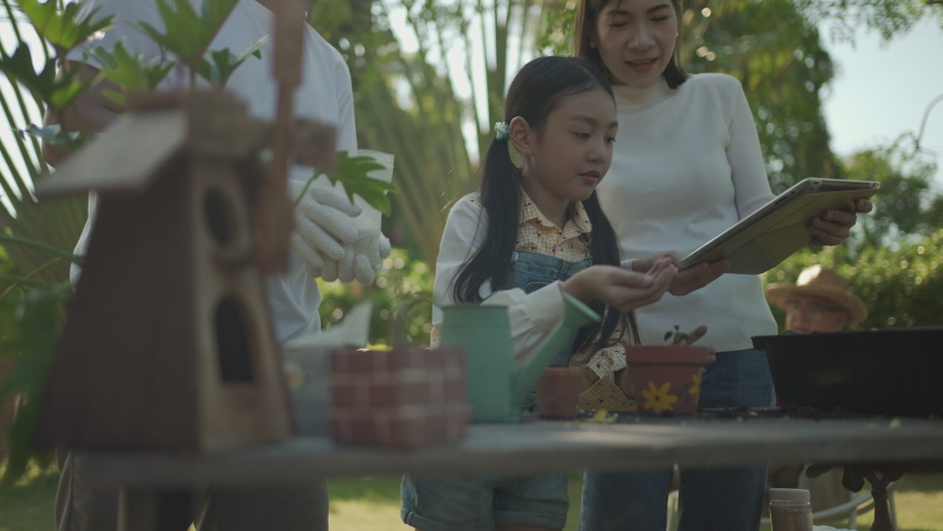 Asian senior couple with granddaughter gardening while watching laptop together in the backyard garden. Happy family gardening together and taking care of nature. People and ecology concept. Royalty-Free Stock Footage #1063225327