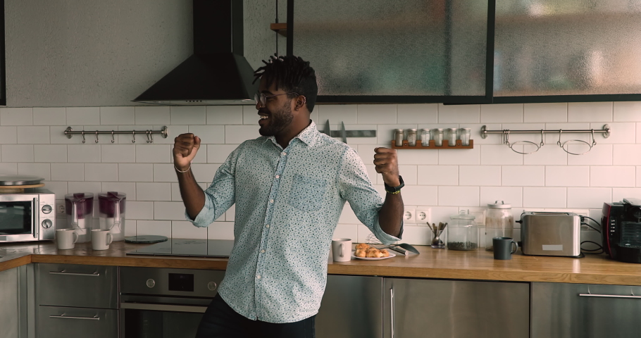 Carefree lively african 30s guy dancing moving while listen hit pop music favourite track spend morning time having fun enjoy new day at comfy home. Happy renter, homeowner in modern kitchen concept Royalty-Free Stock Footage #1063225543