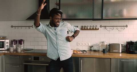 Carefree lively african 30s guy dancing moving while listen hit pop music favourite track spend morning time having fun enjoy new day at comfy home. Happy renter, homeowner in modern kitchen concept
