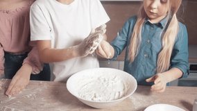 Slow motion adding flour to the dough. Children learn to cook. Flour and dough on the table. Bright kitchen.