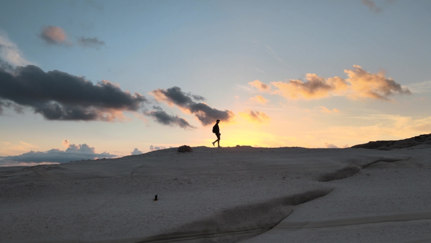 Aerial dolly right shot of the silhouette of a man walking on a rocky landscape against sunset sky