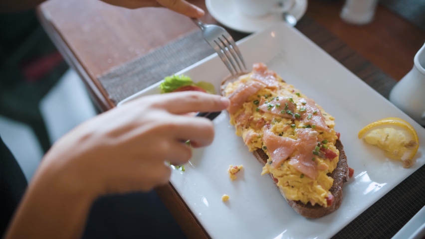 Female cutting and eating a sandwich with salmon and eggs on toasted bread. Woman having breakfast in a cafe top view