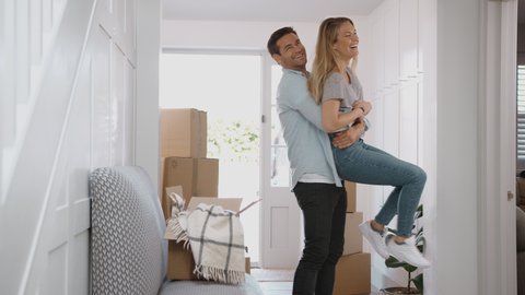 Camera tracks across hallway to show man lifting woman in the air as they move into new home surrounded by boxes - shot in slow motion