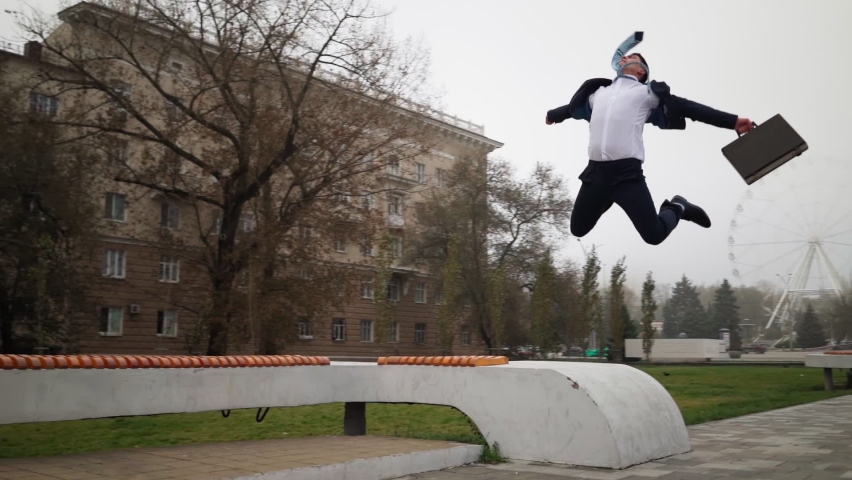 Happy successful businessman in a suit and tie with a suitcase in his hands runs and jumps for joy of victory against the city background. Slow motion. High quality FullHD footage - Powered by Shutterstock - Get 15% off with code: PIKWIZARD15