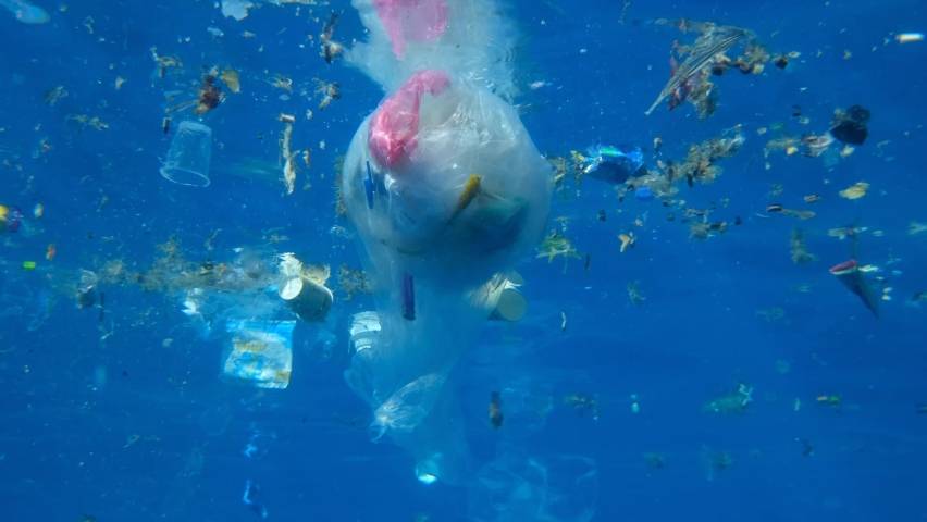 A lot of plastic debris slowly drifting under surface of blue water in sun rays. Plastics bags and cups and other garbage swims underwater. Massive plastic pollution of the Ocean. Slow motion | Shutterstock HD Video #1063229524