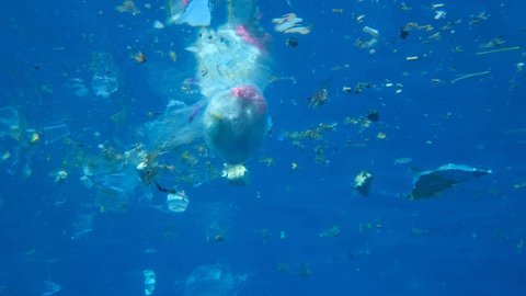 A lot of plastic debris slowly drifting under surface of blue water in sun rays. Plastics bags and cups and other garbage swims underwater. Massive plastic pollution of the Ocean. Slow motion