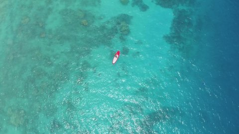 Top view of a lonely red boat sails in the waters of the azure Indian Ocean during calm and sunny weather on a summer day. Tropical tourism concept