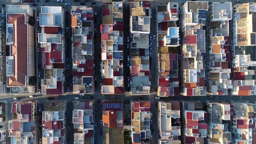 Aerial top down view of city building block located in metropolitan town flight over roofs and streets with vehicles driving around filmed by drone moving up slowly showing more of urban environment