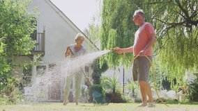 Retired senior man at work watering plants with hose sprays woman tidying garden with rake at home - shot in slow motion - Powered by Shutterstock - Get 15% off with code: PIKWIZARD15