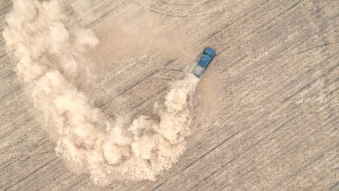 Aerial shot of powerful pickup drifting on dry ground. Black off road vehicle showing performance leaving trace and dust behind. SUV fastly starting ride at the field. Car drive at meadow. Top view