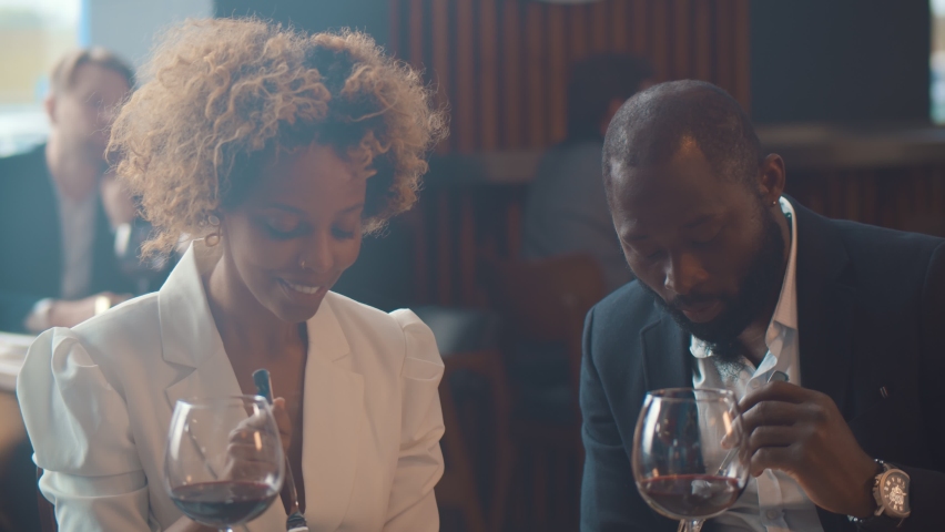 Loving black couple having dinner date feeding each other sitting in restaurant. Portrait of happy elegant african man and woman drinking wine and dining in modern restaurant Royalty-Free Stock Footage #1063232992