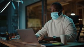 Black African American Man Wearing a Face Mask while Having Online Conversation on a Laptop Computer in Creative Agency. Social Restrictions Concept in Business Office During Coronavirus Pandemic. - Powered by Shutterstock - Get 15% off with code: PIKWIZARD15
