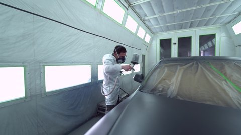 Car body painter spraying car in paint booth