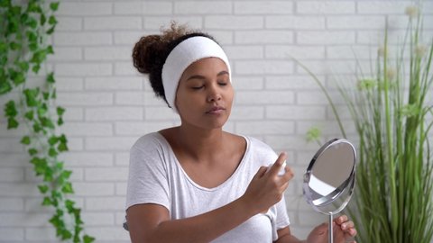 Young woman with eyes closed spraying facial mist at home
