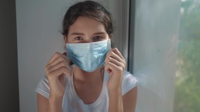coronavirus pandemic concept. little teenage girl takes off medical mask and smiles a beautiful sunlight from the window. self-isolation concept virus covid 19 infection doomsday. Sick child kid - Powered by Shutterstock - Get 15% off with code: PIKWIZARD15