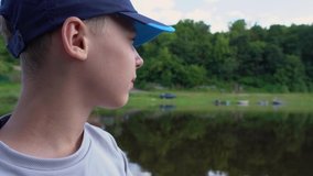 Closeup view 4k video profile portrait of white happy young kid sitting in small motor boat riding along narrow river in scenic summer green landscape. 