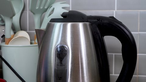 hand turns on the electric kettle for boiling water on kitchen table at home. Making tea or coffee in morning