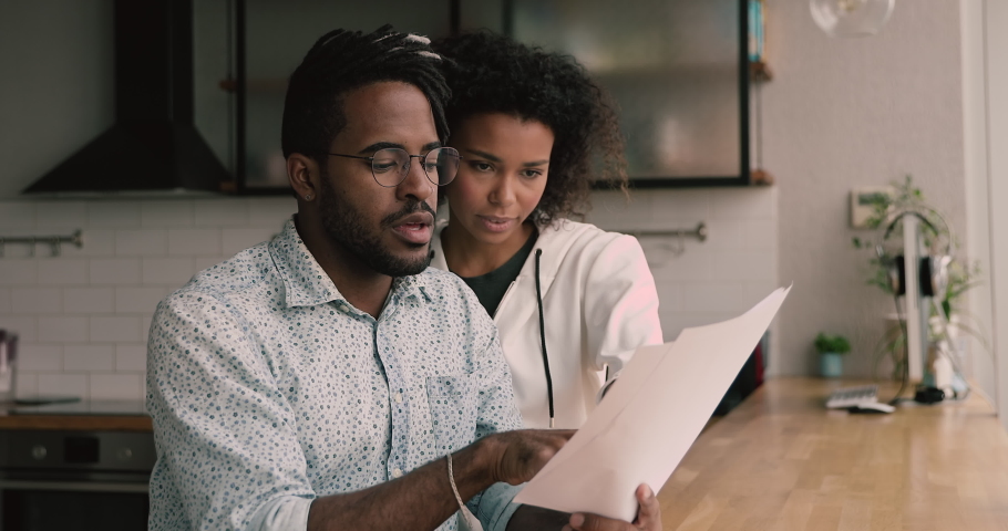 African married young couple holding papers read received correspondence letter document sit at apartment in kitchen, manage family finances, discuss money spend, expenses, get info about taxes refund