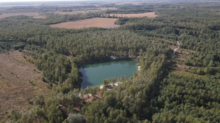 The lake is in the center of the frame, trees are growing around. Around the trees field. the water in the canyon is birch-colored. The lake was filmed from a drone.