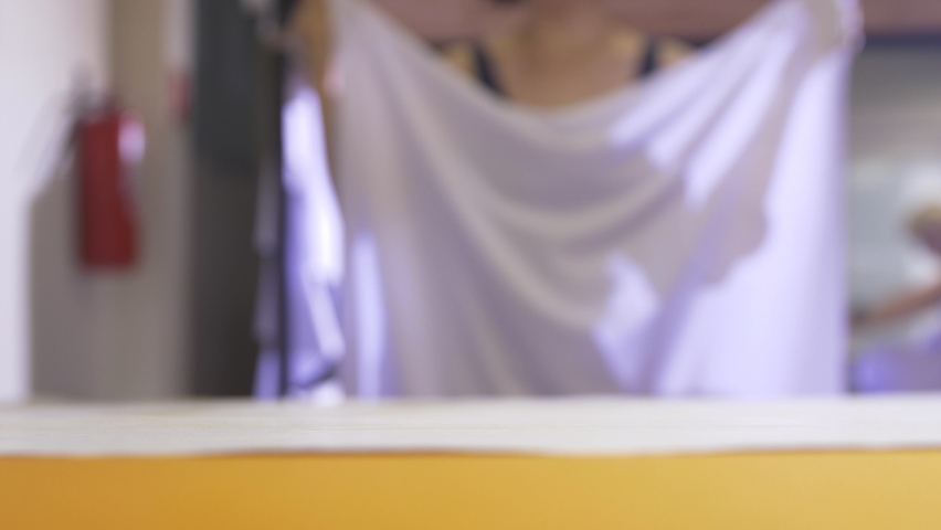 Skilled seamstress puts large sheet of white fabric to make sewing patterns onto workbench in workshop closeup slow motion