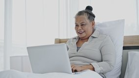 Asian senior woman sitting on a laptop Or happy notebook On white bed in the house or hotel. Finding Healthcare Information, Shopping Online And video conference. Tele consultation with a doctor
