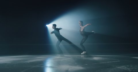 Cinematic shot of young couple of artistic figure skaters is performing a pair skating choreography on ice rink before start of a competition. Concept of perfection, precision, freedom, passion.