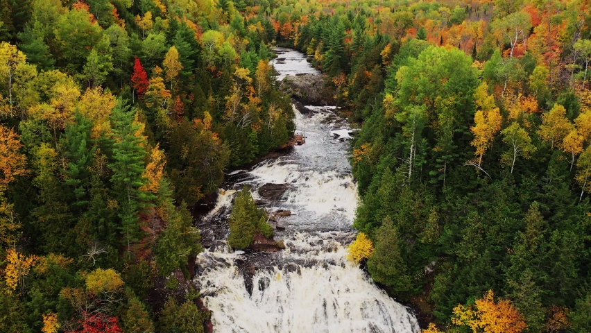 Beautiful autumn aerial flying above the Potato River between the colorful fall tree foliage lining the river with both Lower and Upper Potato River Falls waterfall cascades and rapids below.
