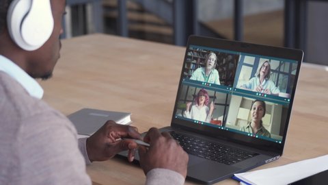 African business man having virtual team meeting on video conference call using laptop working from home office talking to diverse colleagues in remote videoconference online chat. Over shoulder view