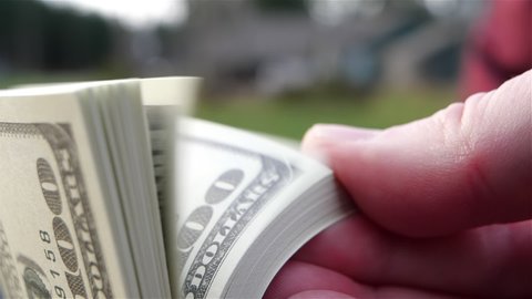 Close-up of a male hand flipping through a stack of 100 dollar bills USD