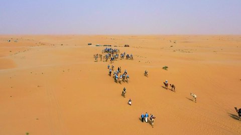 Aerial view over a group of people, riding camels on the Arabian desert, during golden hour, in Saudi Arabia - dolly, drone shot