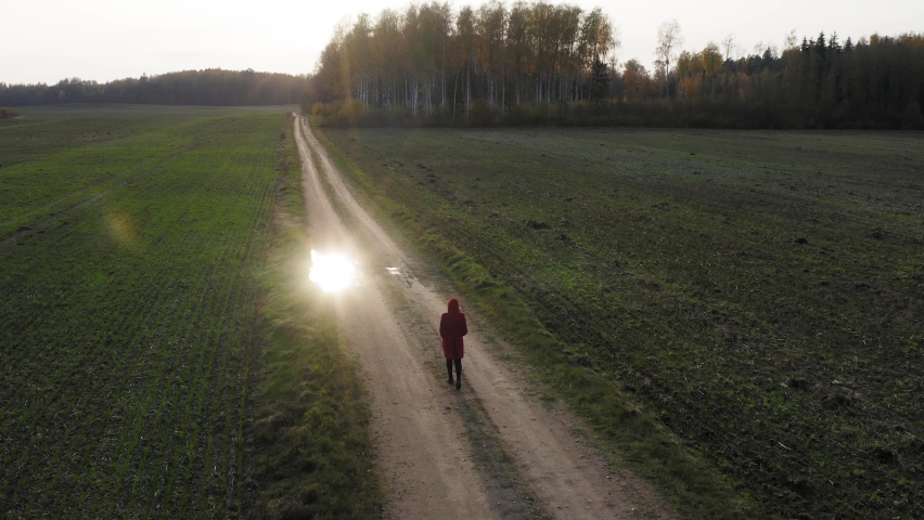 Aerial follow lonely red coat girl walking on pathway beside green field Royalty-Free Stock Footage #1063247539