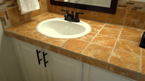 Bathroom sinks with dark brown faucets and mosaic tile countertop and backsplash. Traditional bathroom interior design with white over mount single bowl sink.